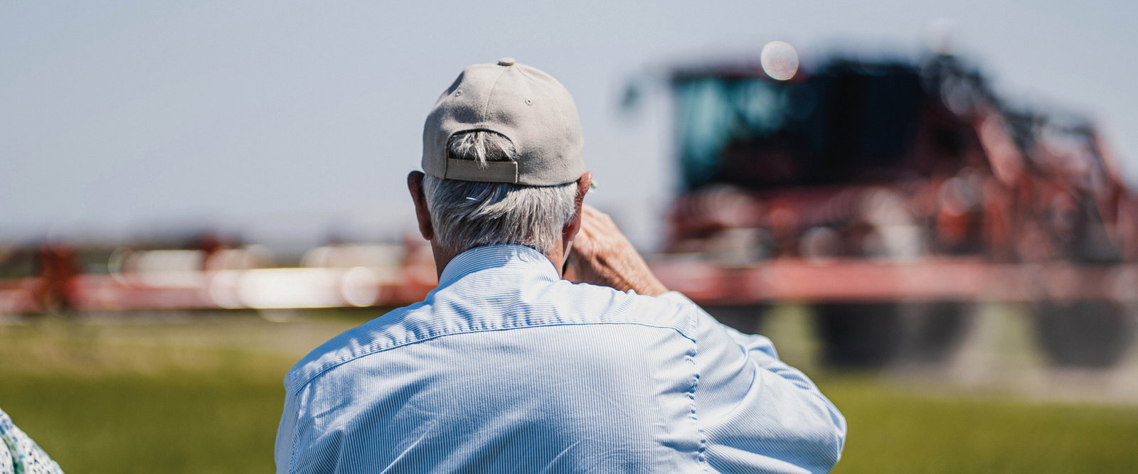 Man wearing a cap looking at a sprayer in the distance.