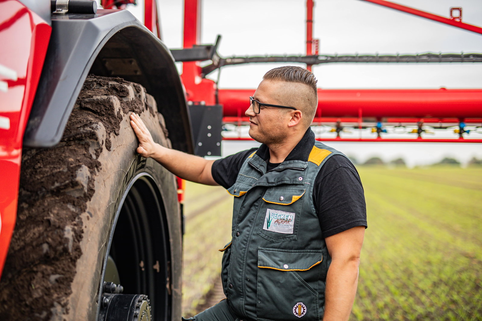 A man wearing a black shirt and glasses stands beside an Agrifac sprayer, showcasing a rural or agricultural setting.