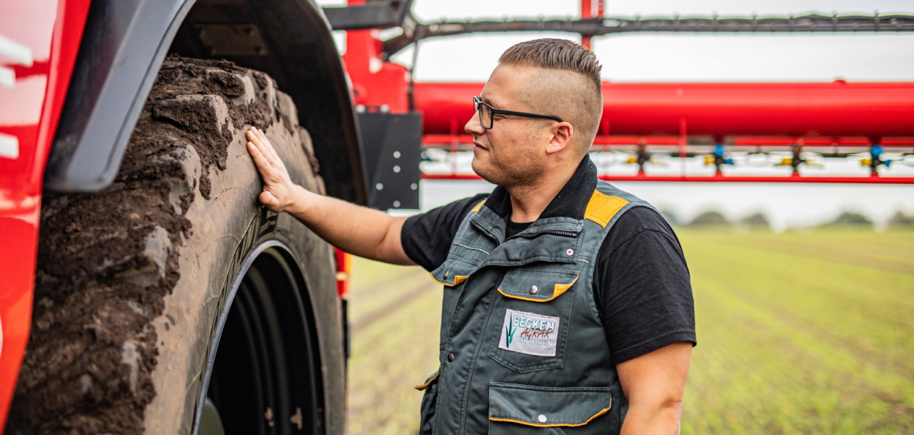 A man wearing a black shirt and glasses stands beside an Agrifac sprayer, showcasing a rural or agricultural setting.