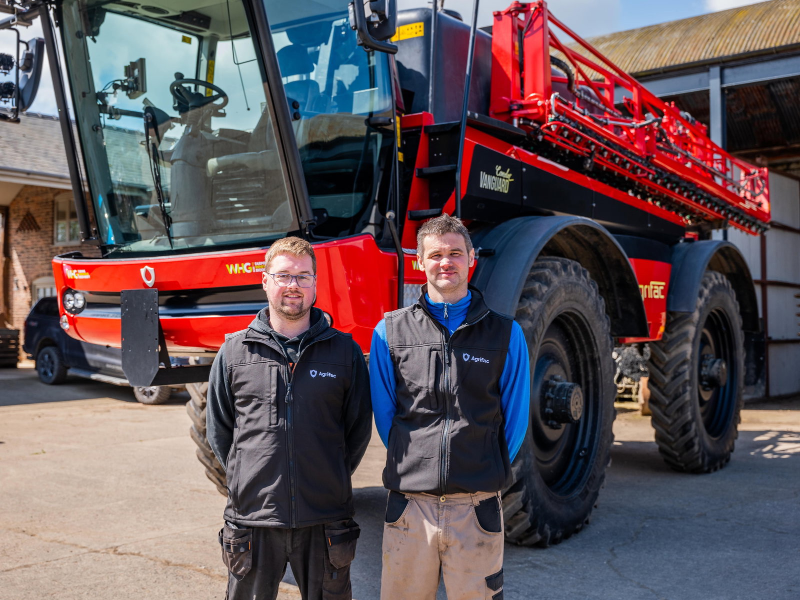 Two men stand beside an Agrifac sprayer, showcasing its size and machinery in an outdoor setting.