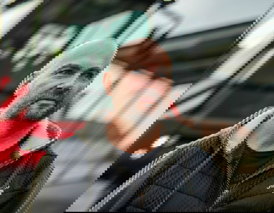A bald man stands confidently in front of a bright red Agrifac sprayer.