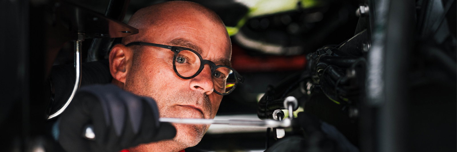 A man wearing glasses and a red shirt is diligently working on an Agrifac sprayer with focused attention.