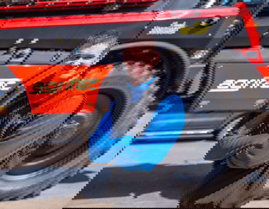 A man stands confidently in front of an Agrifac sprayer, showcasing its impressive size and machinery.